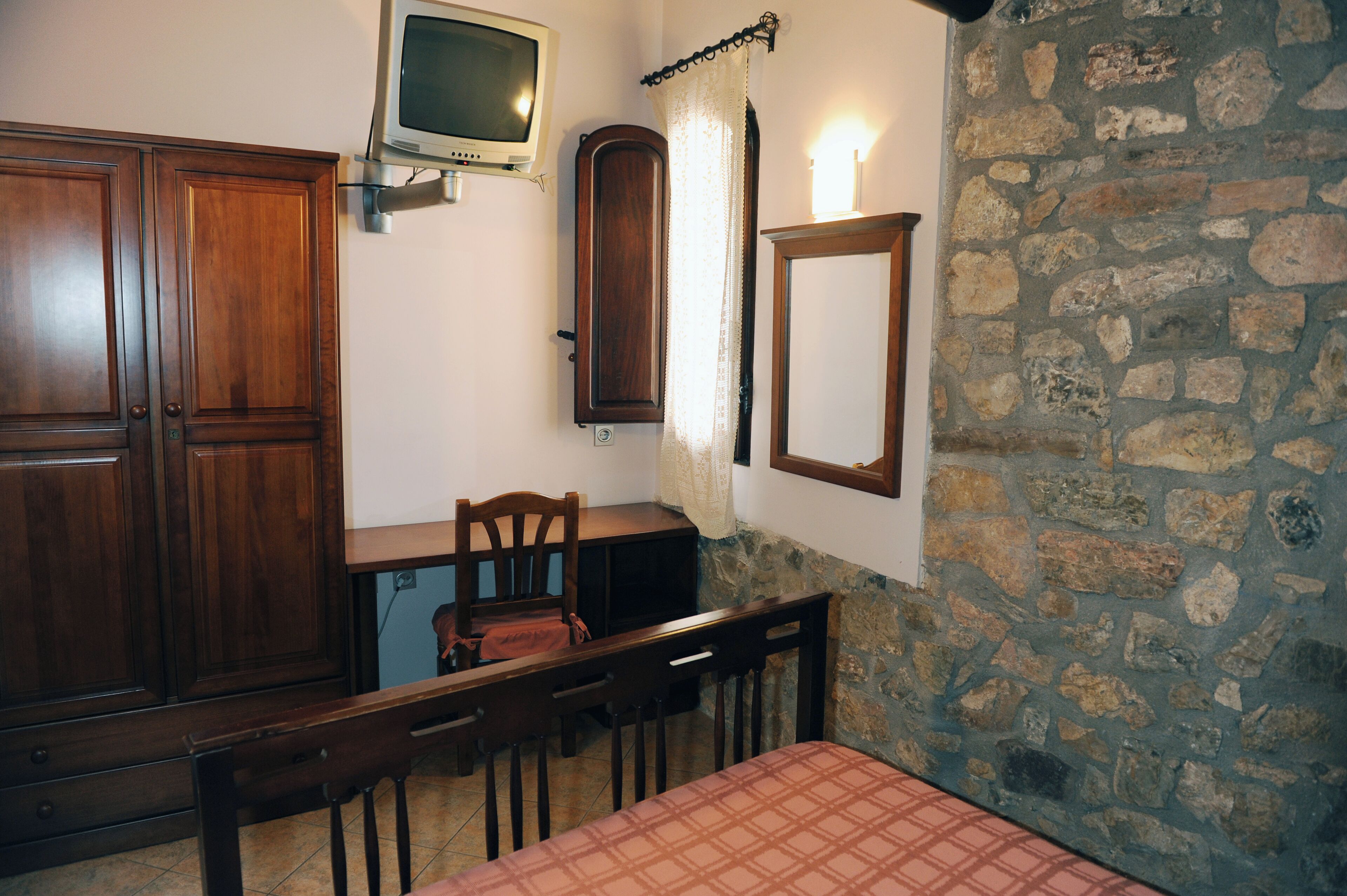 A room with a stone wall, wooden furniture, a television, and a mirror.