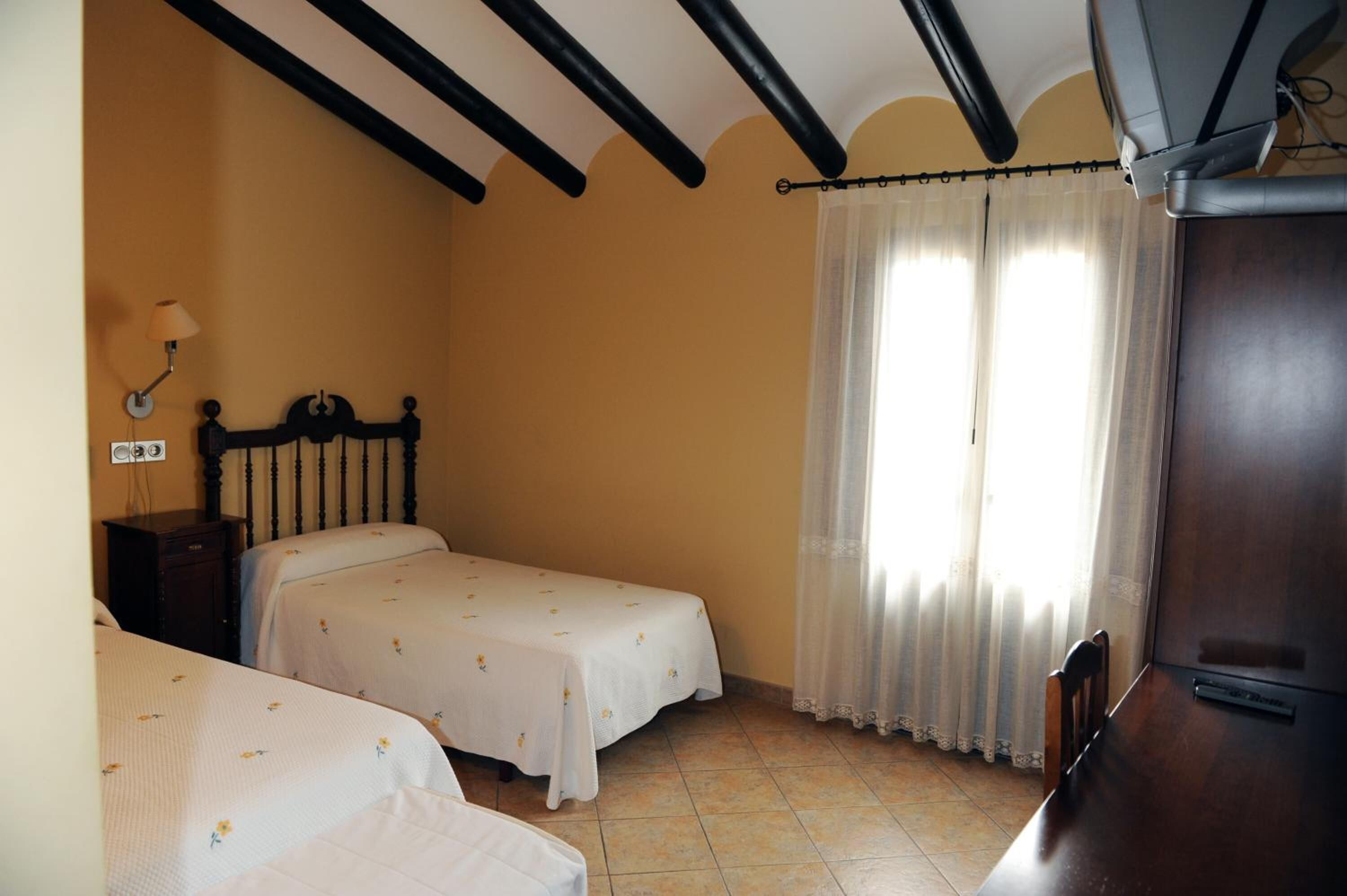 Un dormitorio con dos camas, un armario de madera, un escritorio y una ventana con cortinas.
