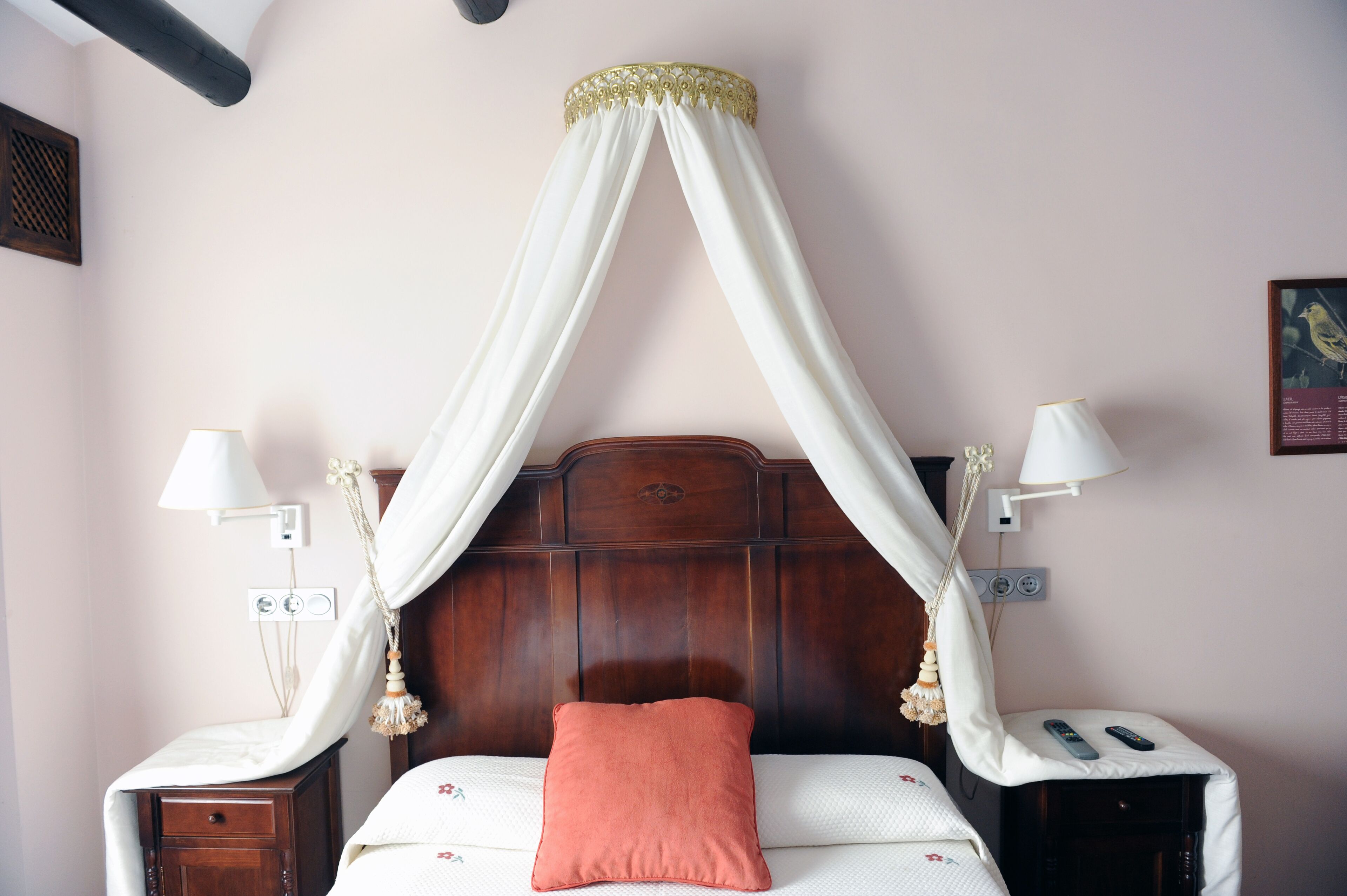 A bedroom with a four-poster bed, bedside lamps, a nightstand, and a wall-mounted power outlet.