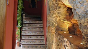 Una escalera con peldaños decorados que lleva a una habitación con pared de piedra y una planta colgante.