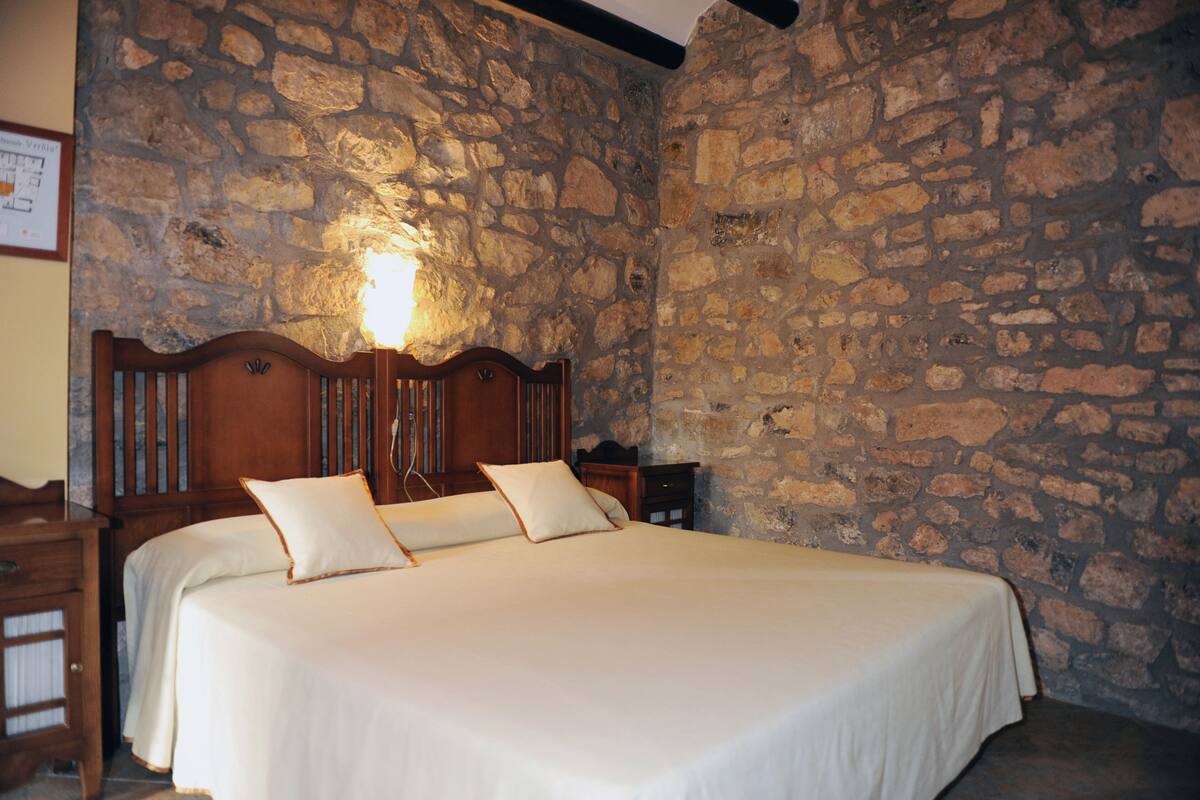 A bedroom with a stone wall, a wooden bed frame, and a nightstand.