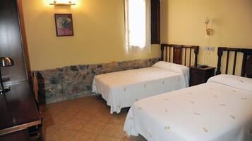 A room with two beds, a wooden cabinet, a stone wall, and a window with a curtain.