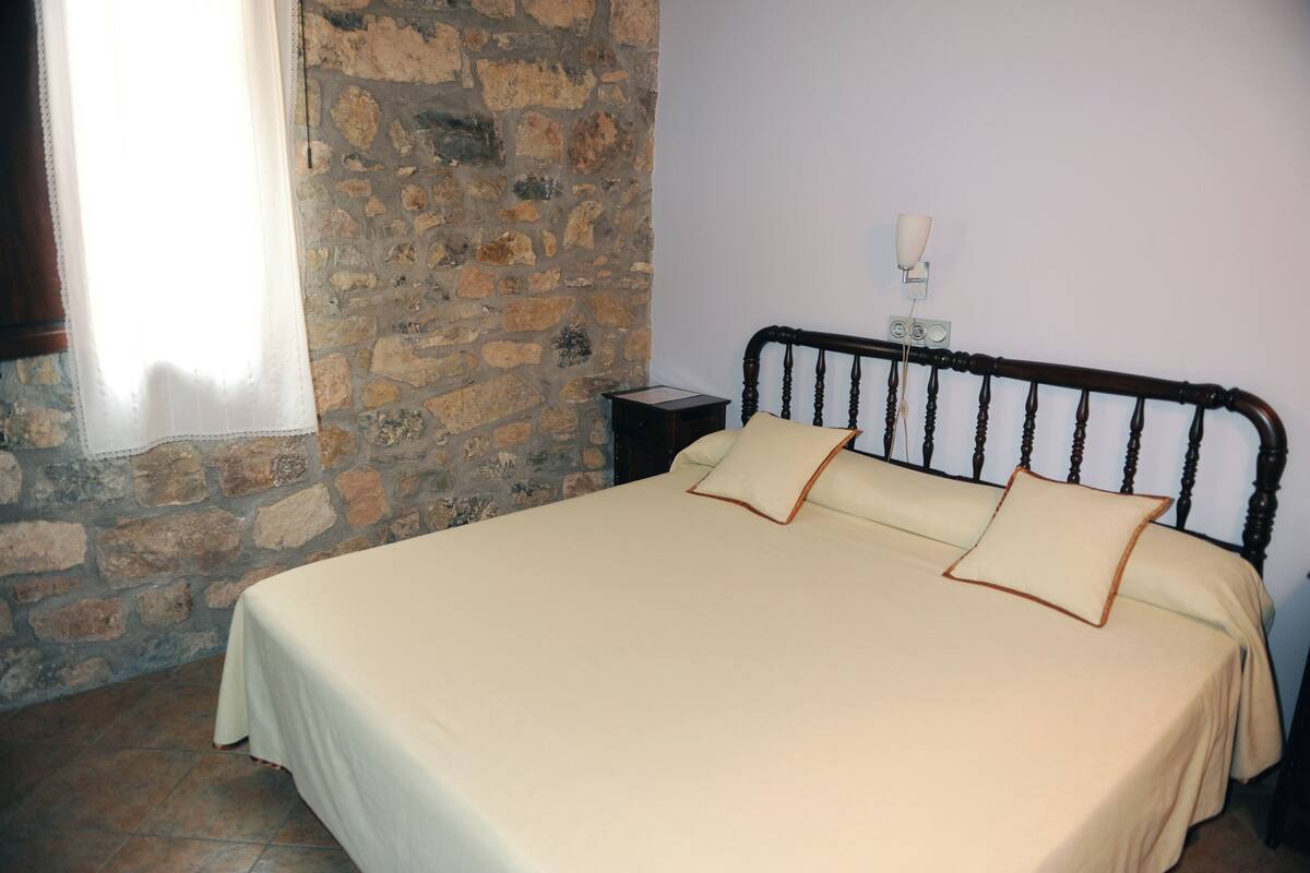A bed with a wooden headboard, a stone wall, and a nightstand with a lamp.