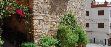 Un bâtiment en pierre doté d’un balcon, de plantes en pot et situé sur une rue pavée.