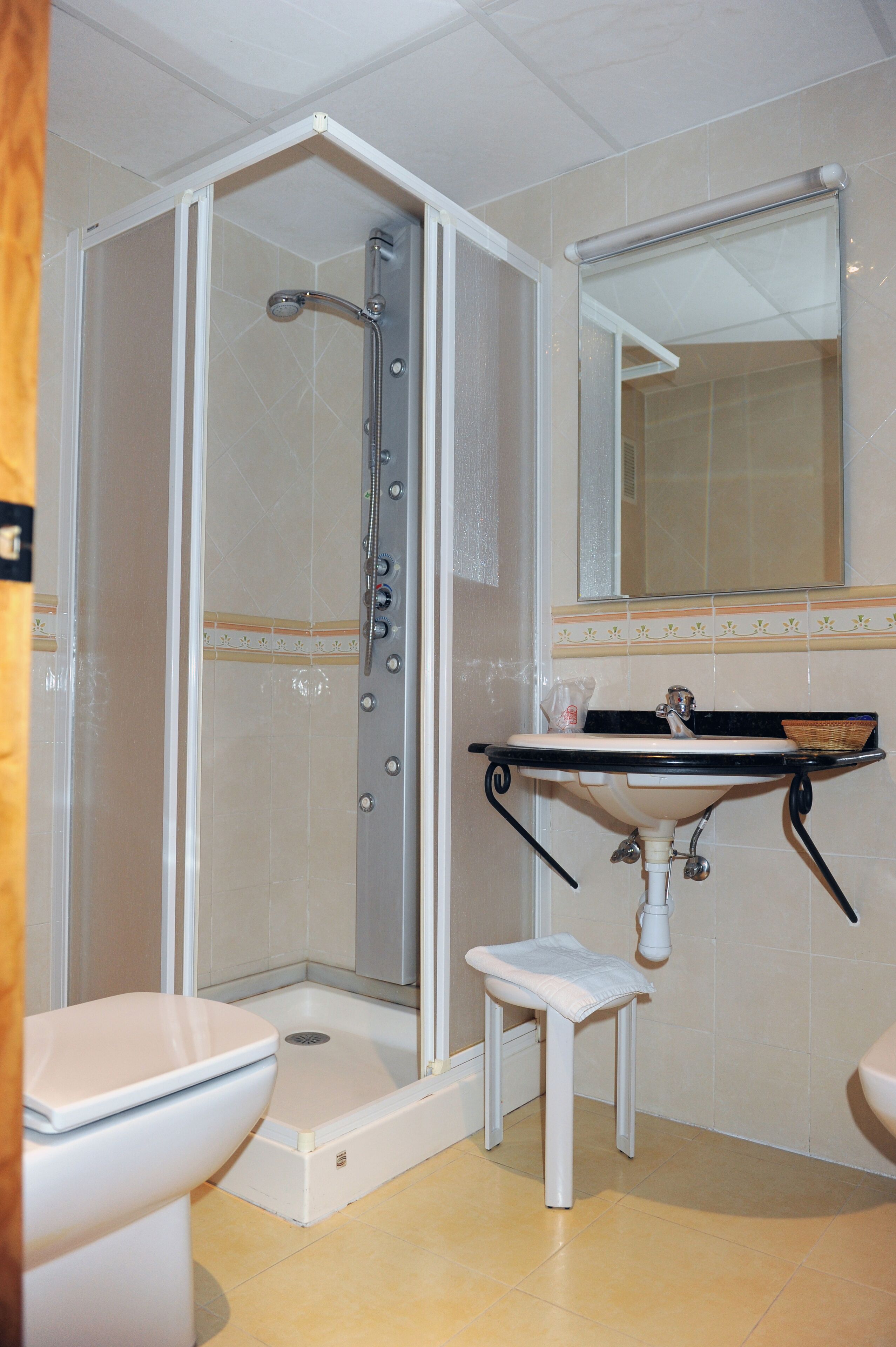 A bathroom with a shower, toilet, sink, and a small stool.