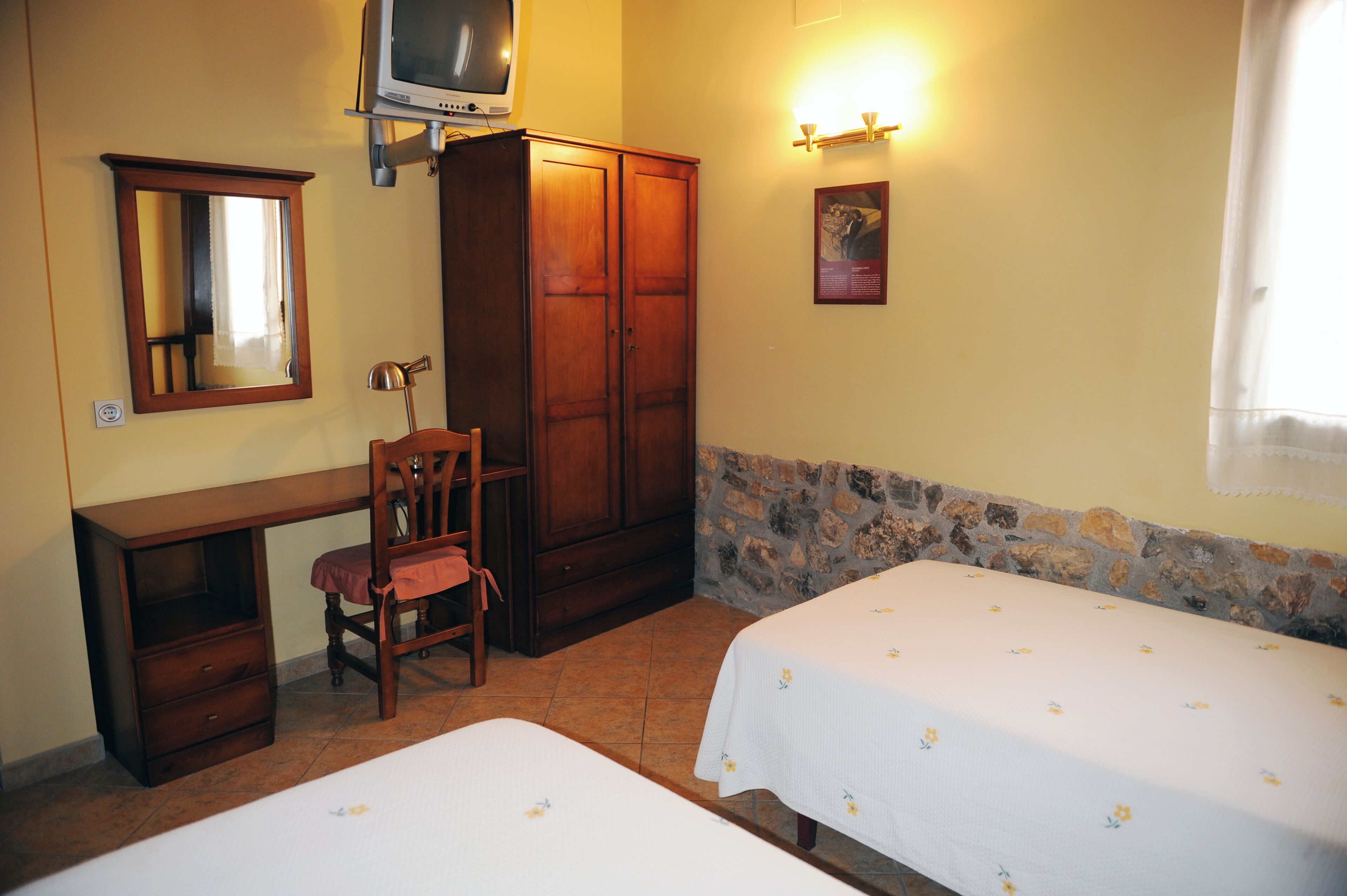 A room with a desk, chair, wardrobe, and two beds.