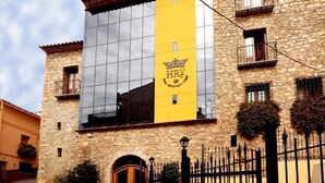 Un edificio de piedra con una franja vertical amarilla y el logotipo de una corona, que indica un hotel o restaurante.