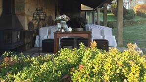 An outdoor seating area with a stone wall, a table with a vase of flowers, and a covered patio with chairs. - Casa Grande de Fuentemayor (Silleda)