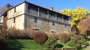 A stone building with a balcony, surrounded by well-maintained hedges and a stone wall. - Casa Grande de Fuentemayor (Silleda)