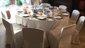 A round dining table set for breakfast with white chairs, plates, cups, and glasses of orange juice. - Casa Grande de Fuentemayor (Silleda)