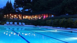 A swimming pool with clear water, surrounded by white chairs and a building with multiple windows and lights. - Casa Grande de Fuentemayor (Silleda)