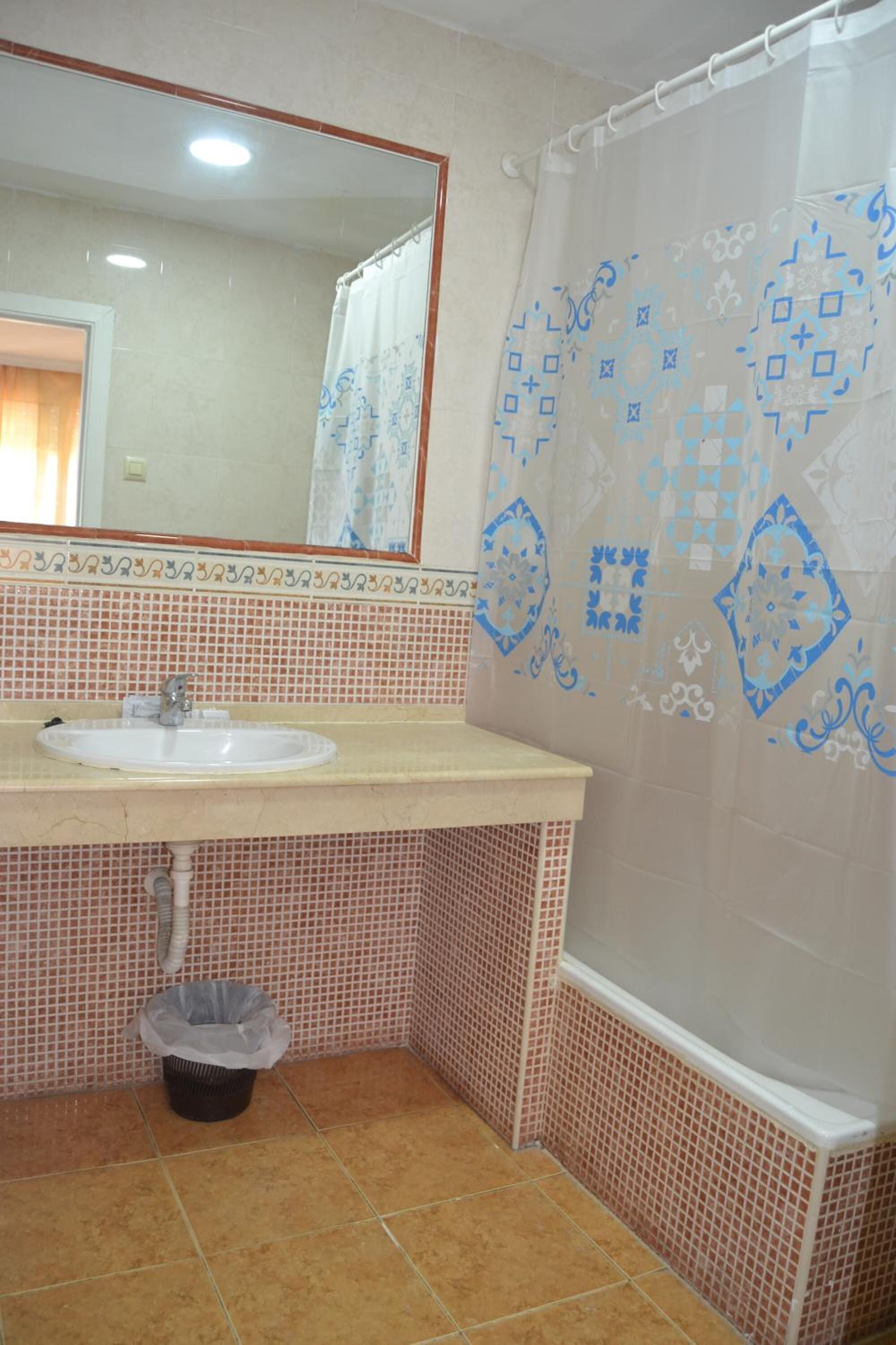 Un baño con lavamanos, espejo, cortina de ducha y paredes de azulejos.