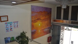 Un espace d’accueil avec un tableau représentant un coucher de soleil, un extincteur et un panneau indiquant l’emplacement de la zone fumeurs.
