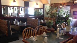 Ein Restaurant mit Sitzecken und Tischen, Holzstühlen und Topfpflanzen.