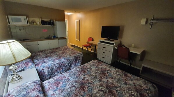 A room with two beds, a desk with a chair, a television, a microwave, and a refrigerator.