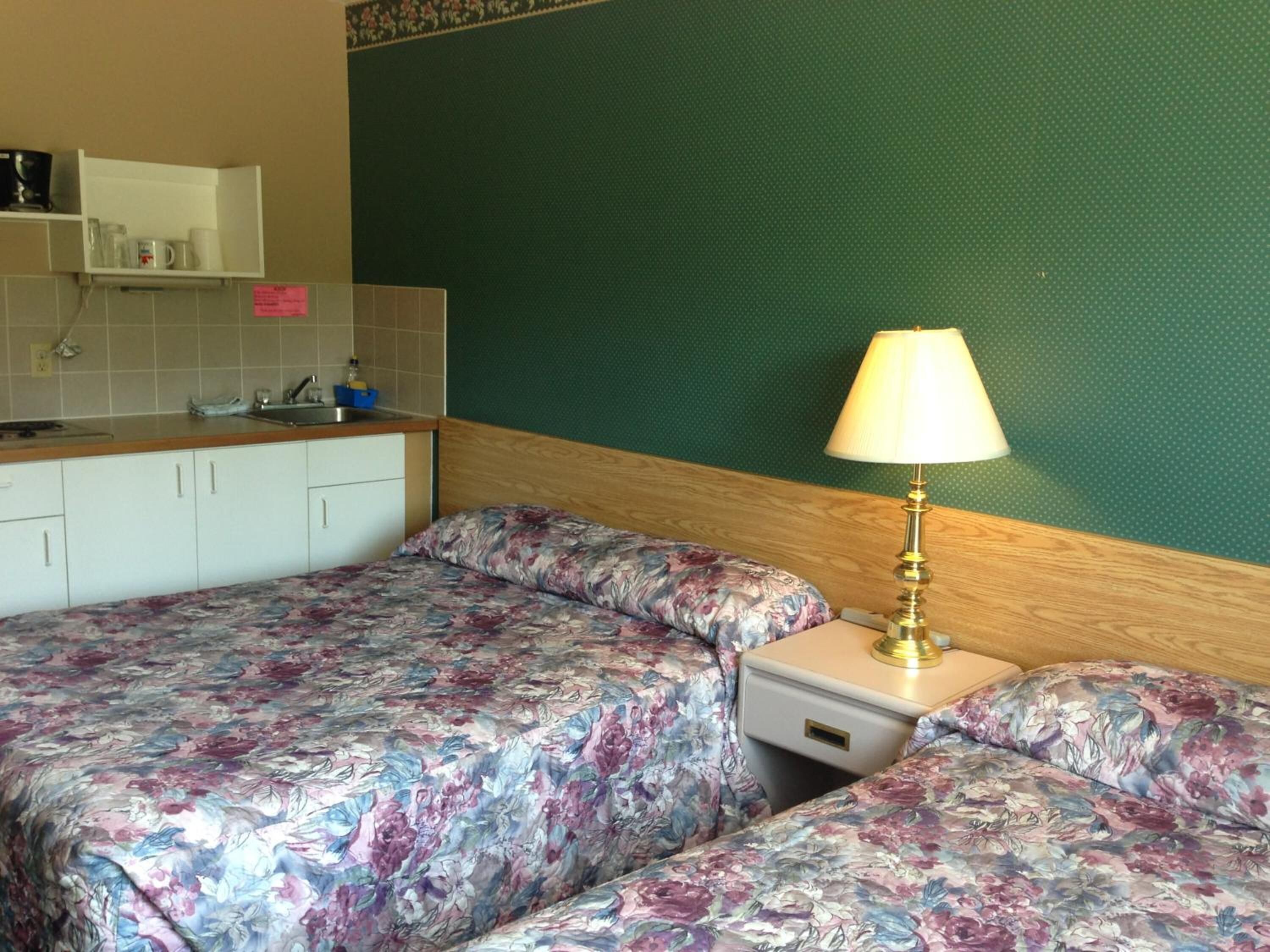 Une chambre avec deux lits, une petite kitchenette et un mur vert.