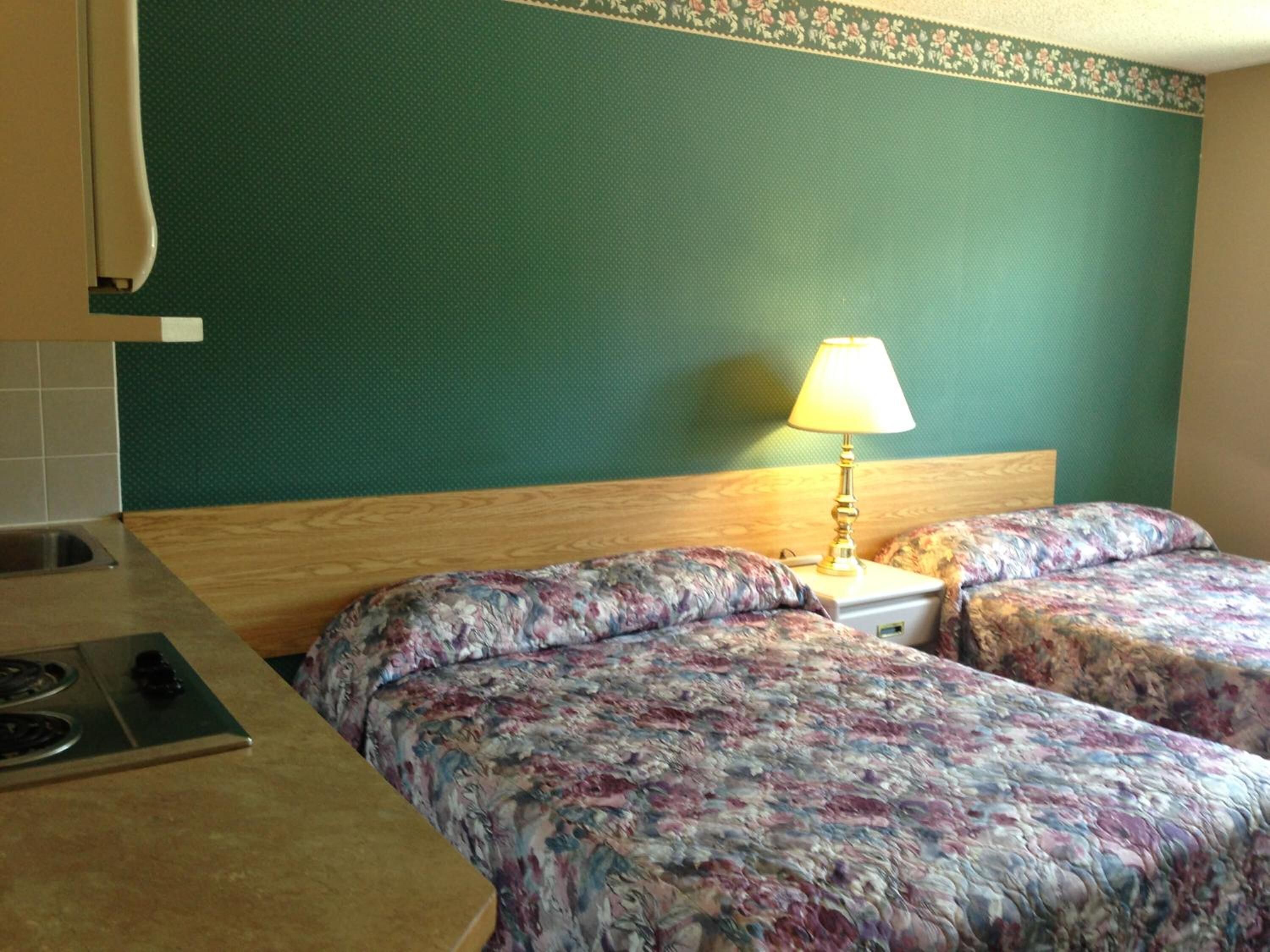 Una camera d'albergo con due letti, un tavolino, una lampada e un angolo cottura con un piano cottura.