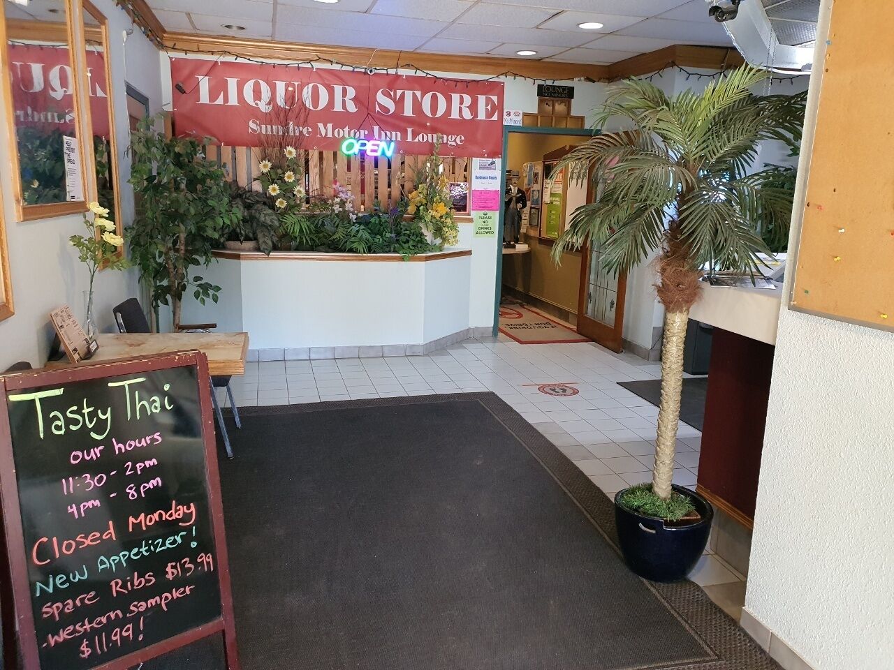 Interior de un restaurante con un letrero de licorería, un menú en la pizarra y una palmera.