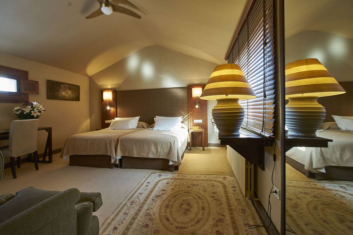 A hotel room with two beds, a desk, a chair, and a large window with blinds.