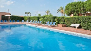 A swimming pool with lounge chairs and a bench, surrounded by greenery and palm trees. - Pierre & Vacances Comarruga (El Vendrell)