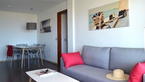 A living room with a grey sofa, red cushions, a white coffee table, and a painting of a sailing boat. - Pierre & Vacances Comarruga (El Vendrell)