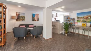 A reception area with a counter, a bookshelf, and two chairs. - Pierre & Vacances Comarruga (El Vendrell)