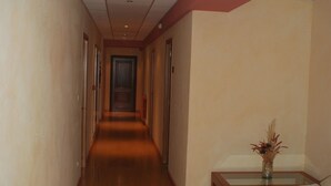 A hotel hallway with wooden flooring, a sofa, a small table with a vase, and a door at the end. - Hotel Canabal (Burela)