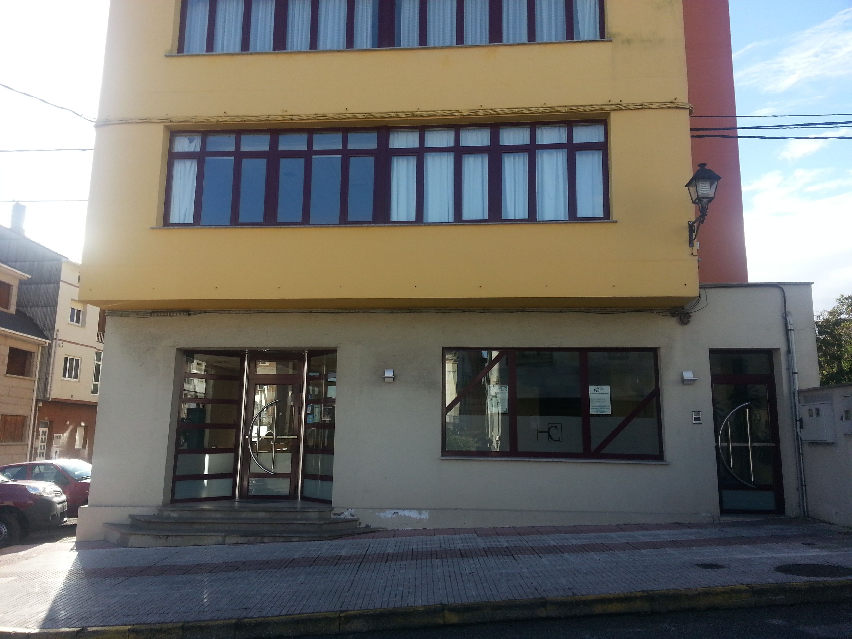 Un edificio de dos pisos con fachada amarilla y un detalle rojo a la derecha.