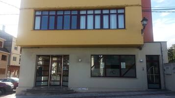 Un edificio de dos pisos con fachada amarilla y un detalle rojo a la derecha.