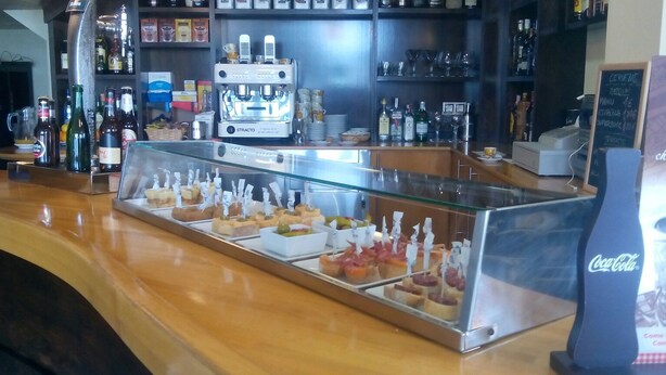 A bar area with a coffee machine, shelves with bottles, and a display case with snacks. - Hotel Canabal (Burela)