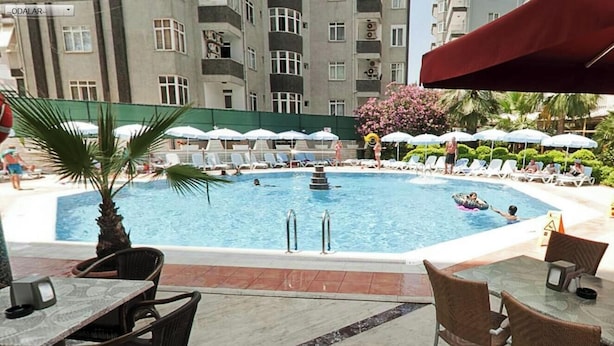 A swimming pool with lounge chairs and umbrellas, surrounded by a building with balconies. - Carmen Suite Hotel (Alanya)