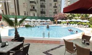 Una piscina con tumbonas y sombrillas, rodeada por un edificio con balcones.