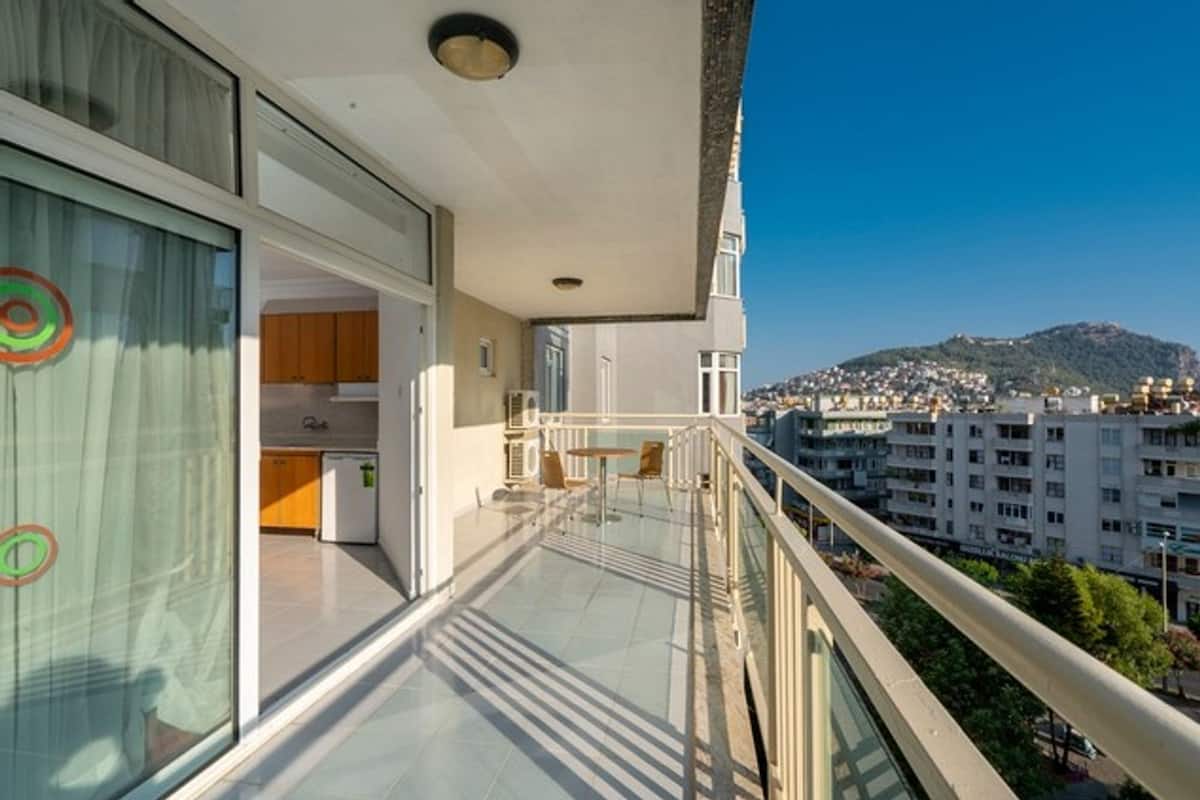 Ein Balkon mit Glastrennwand mit Blick auf eine Stadtlandschaft und ein Gebirge.