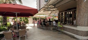 An outdoor patio area with tables and chairs, umbrellas, and a bar with a tiled wall.
