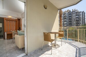 A balcony with a table and chairs, a sliding door leading to a room, and a view of a multi-story building. - Carmen Suite Hotel (Alanya)