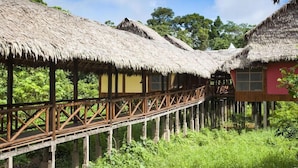 A wooden walkway connecting traditional thatched-roof huts in a lush, green environment. - Heliconia Amazon River Lodge (Indiana)