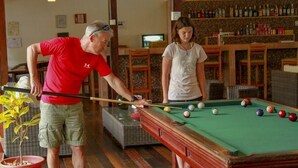 A pool table in a room with wooden flooring, a bar area with bottles, and a potted plant. - Heliconia Amazon River Lodge (Indiana)