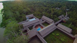 A traditional thatched-roof structure with a central courtyard and a small pool, surrounded by dense forest and a body of water. - Heliconia Amazon River Lodge (Indiana)