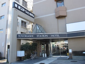 L’entrée de l’hôtel Toyohashi Station, avec sa façade en verre transparent, un vélo garé à l’extérieur et une enseigne indiquant le nom de l’hôtel.