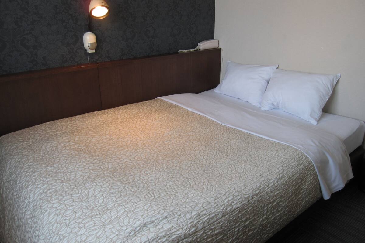 A neatly made bed with a white bedspread and pillows, a bedside lamp, and a telephone on the nightstand.