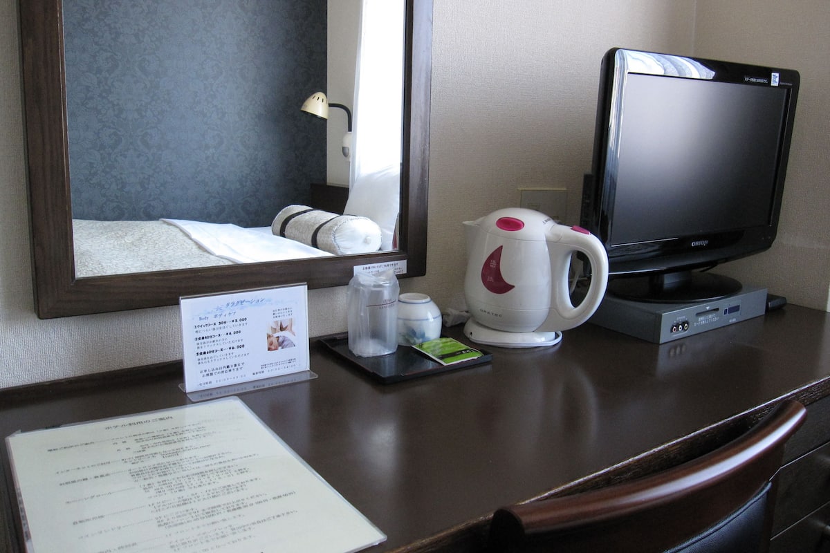 A hotel room with a bed, a television, a kettle, and a menu on the table.