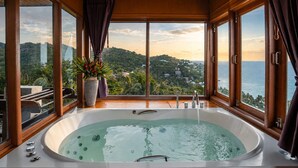 A large bathtub with a view of a mountainous landscape and the sea.