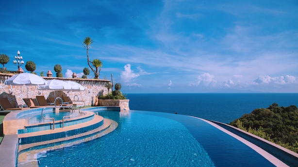 A infinity pool with a stone wall and lounge chairs, overlooking a clear blue sea.