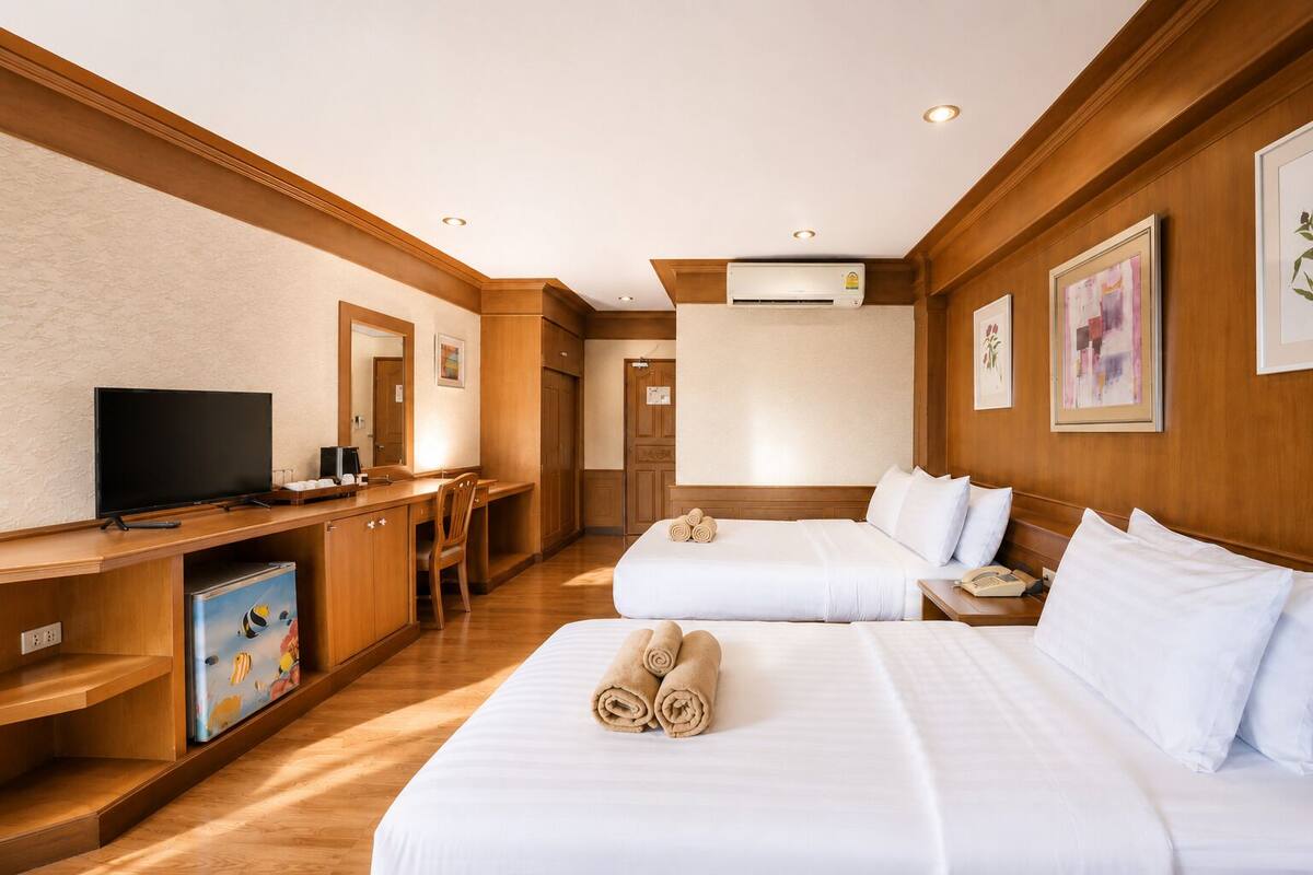 Ein Hotelzimmer mit zwei Betten, einem Schreibtisch mit Fernseher, einem kleinen Kühlschrank und einer Klimaanlage.