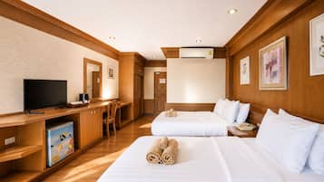 A hotel room with two beds, a desk with a television, a small refrigerator, and an air conditioning unit.