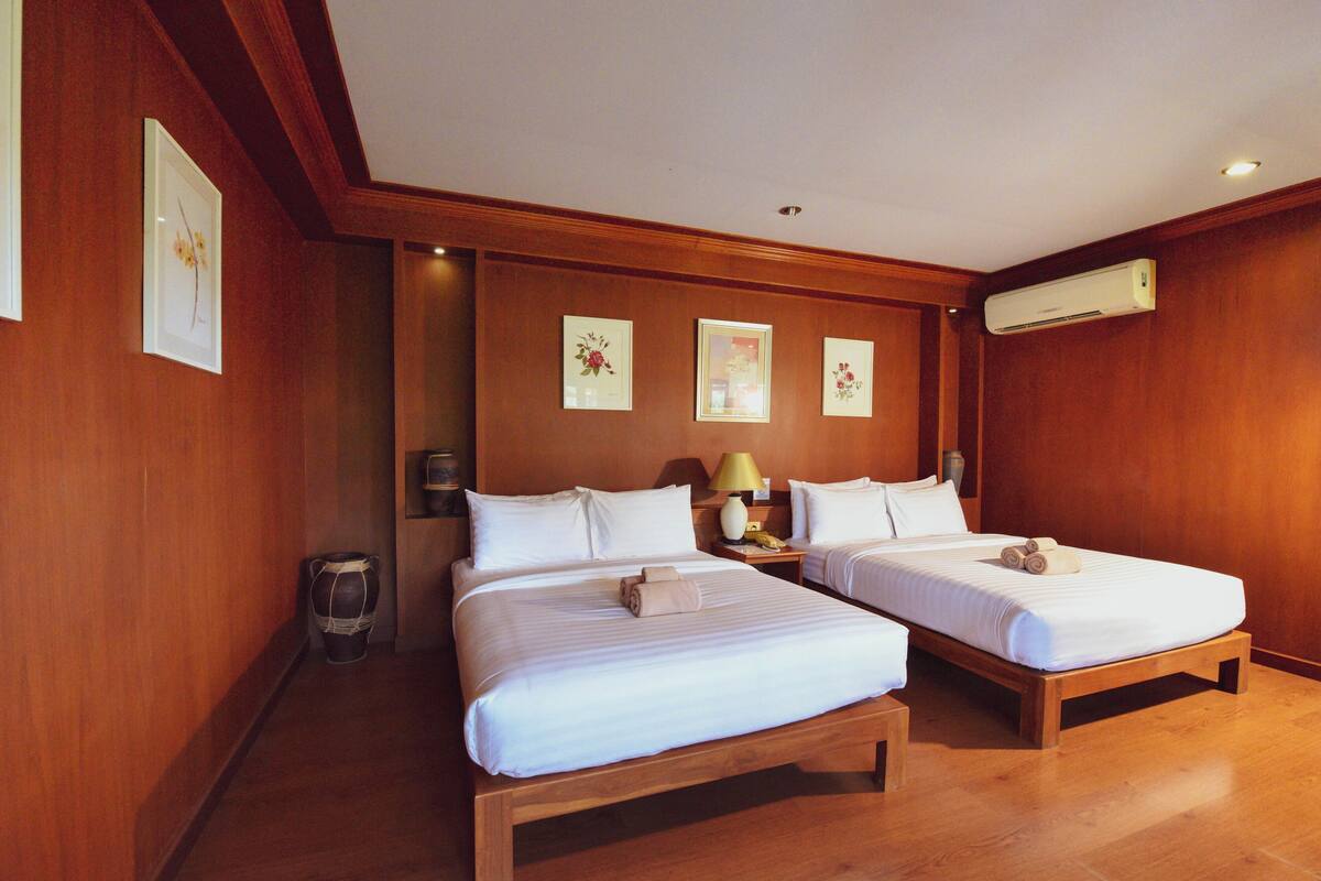 Ein Hotelzimmer mit zwei Betten, Holzboden, einer Wand-Klimaanlage und gerahmten Kunstwerken.
