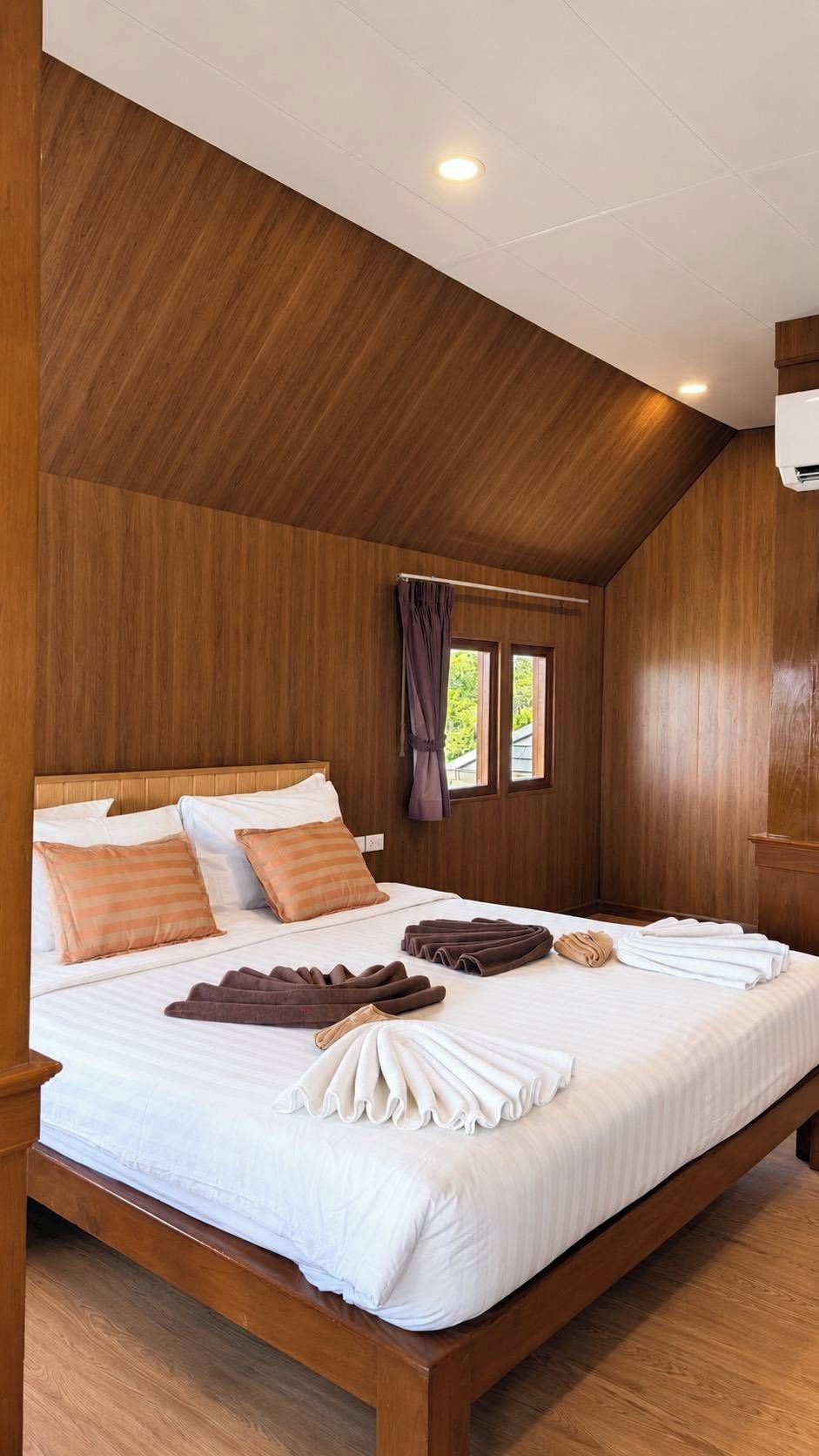 A bedroom with a wooden ceiling, a bed with white linens, and a window with curtains.