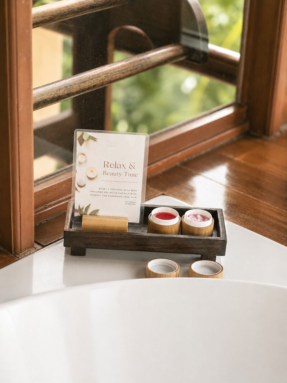 Una bandeja de madera con un letrero que dice 'Relax & Beauty Time' y productos de spa sobre una mesa cerca de una ventana.