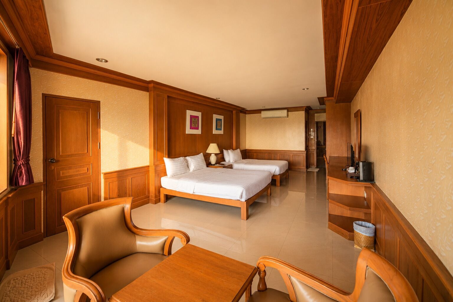 A hotel room with a large bed, two bedside tables, a desk with a chair, a TV, and a door.