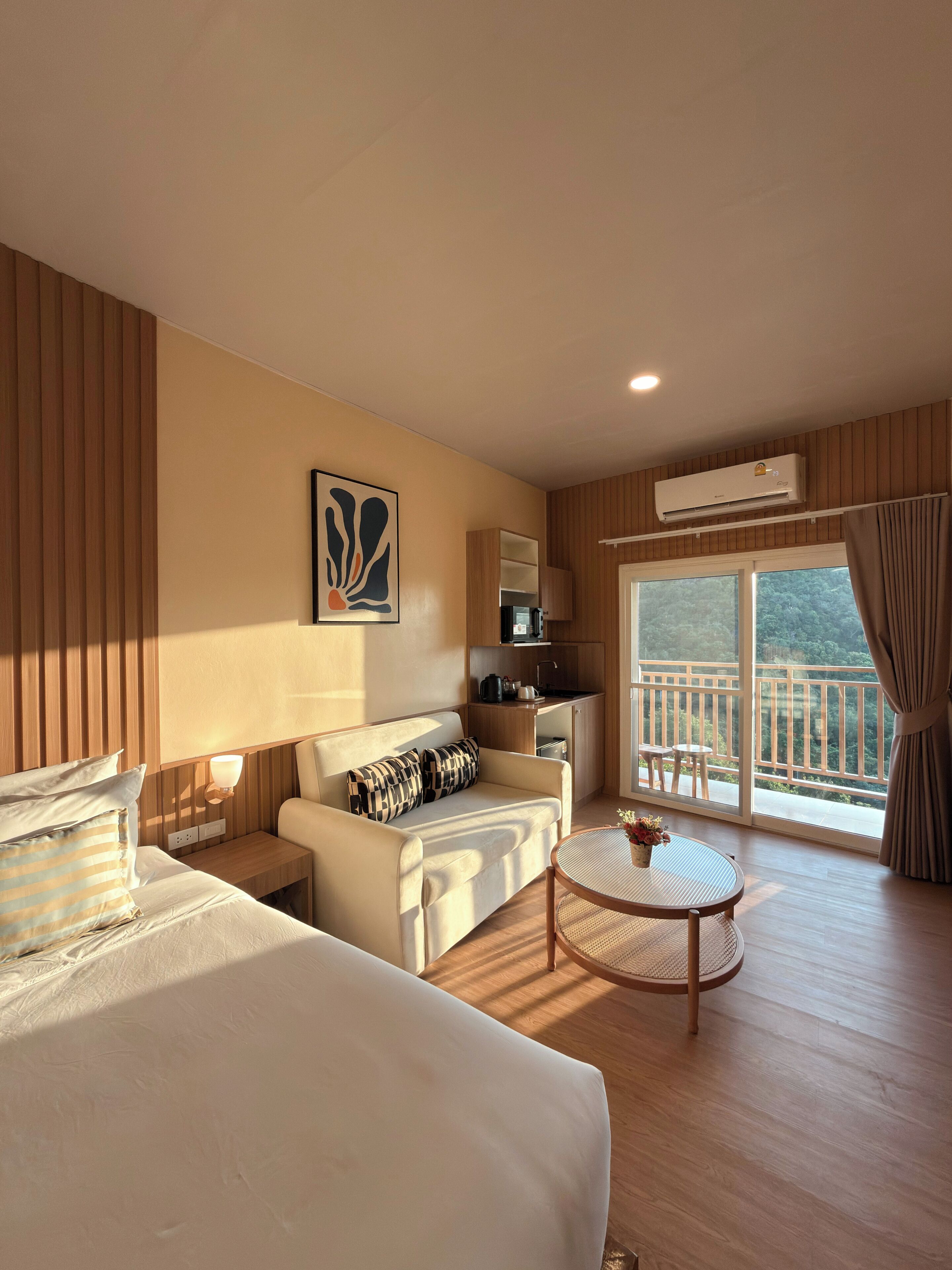 Een hotelkamer met een bed, een slaapbank, een tafeltje, een kitchenette en een balkon met uitzicht.